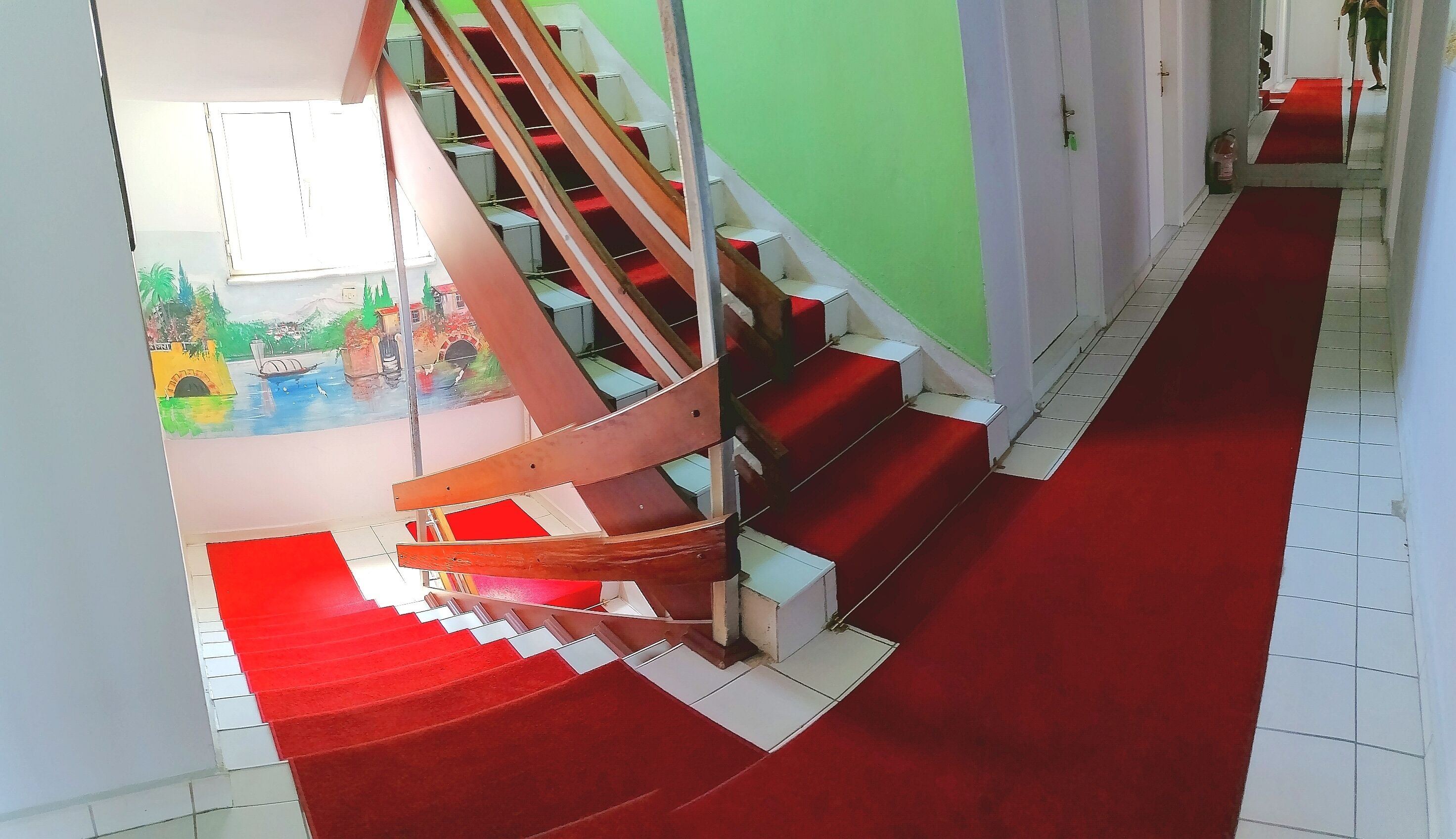A staircase with red carpeted steps leading to a landing with a green wall and a white door.