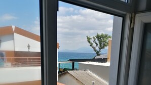 A view through a window of a building with a balcony overlooking a beach and the sea. - Mudanya Otel (Mudanya)