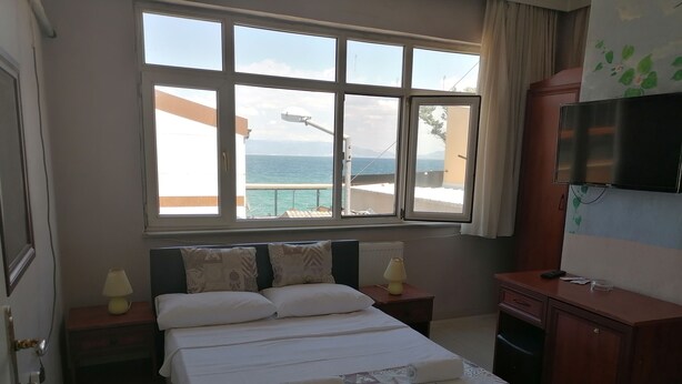 A hotel room with a bed, two bedside tables with lamps, a TV, and a view of the sea. - Mudanya Otel (Mudanya)