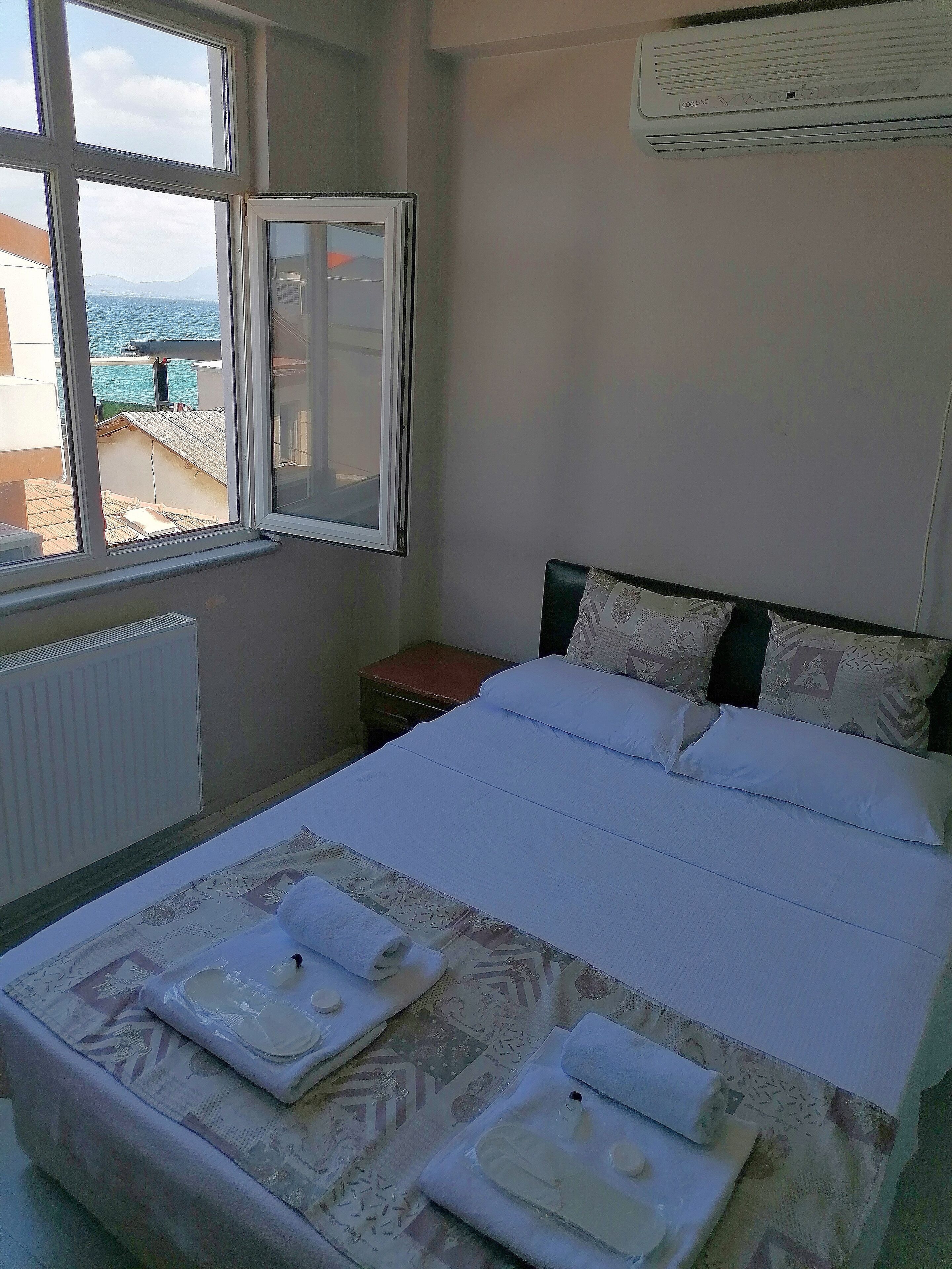A bedroom with a bed, a window with a view of the sea, and an air conditioning unit on the wall.