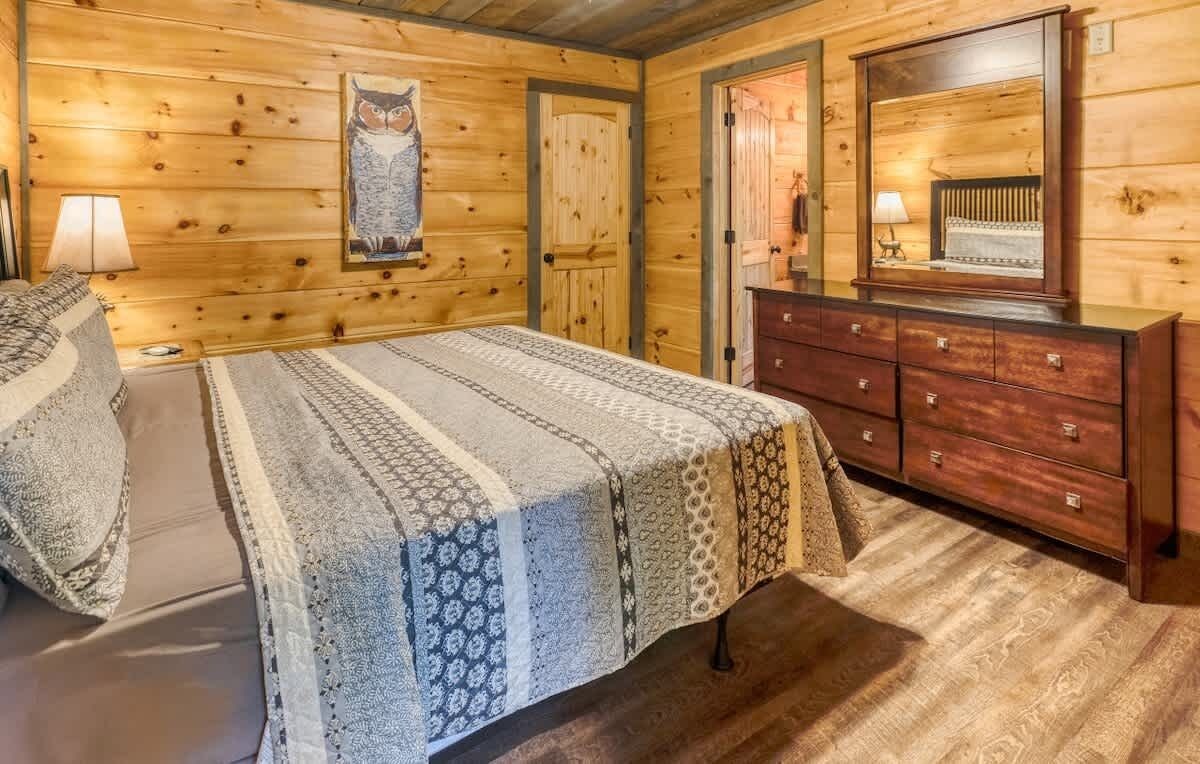 A wooden-paneled room with a bed, dresser, and a mirror.