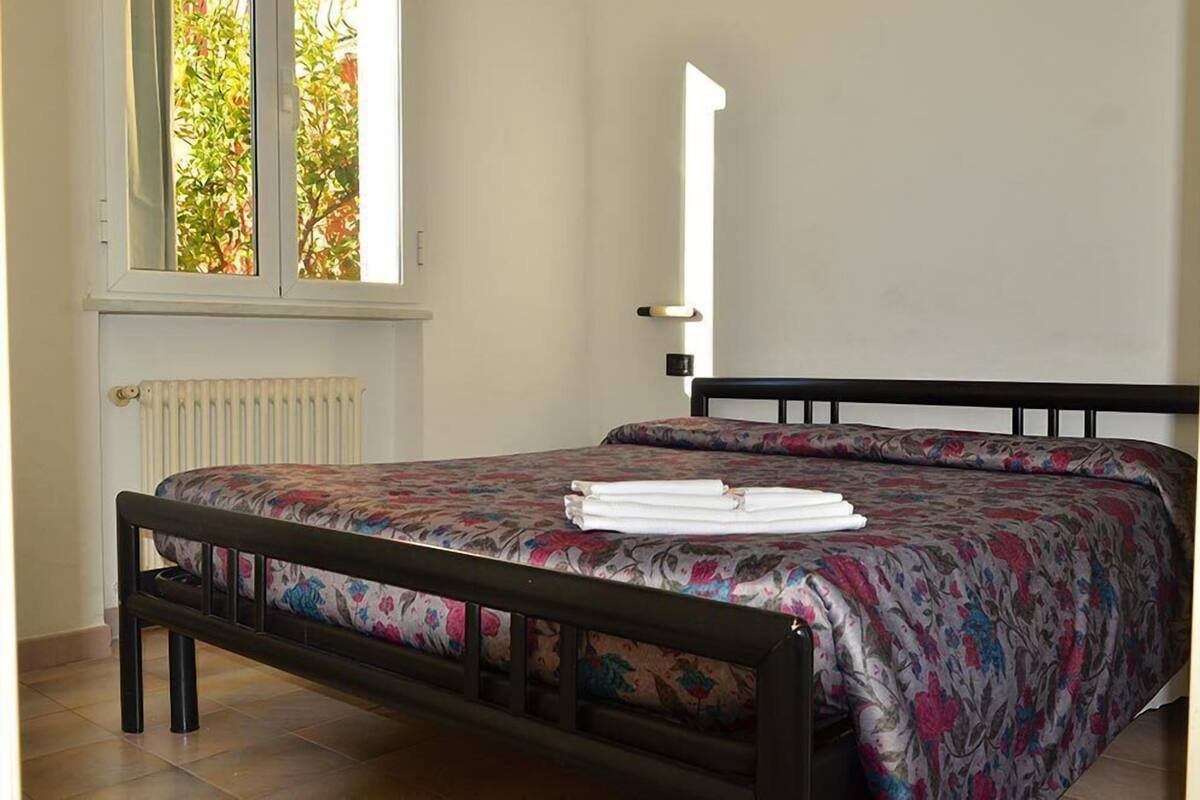 A bedroom with a bed, a radiator, and a window with a view of trees.