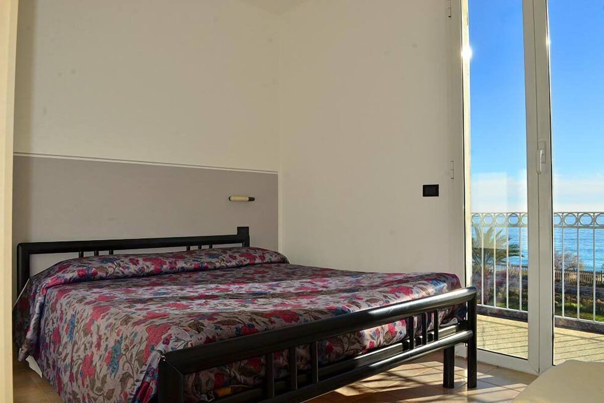 A bedroom with a bed, a window, and a view of the sea.