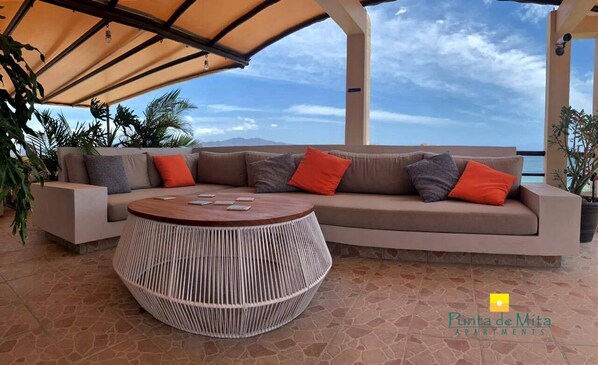 Un espace extérieur aménagé avec une table ronde en fibres tressées, un canapé confortable et une pergola au-dessus.