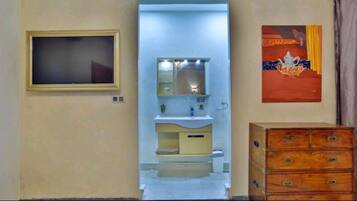 A room with a television on the left, a bathroom with a sink and mirror, and a wooden dresser on the right.