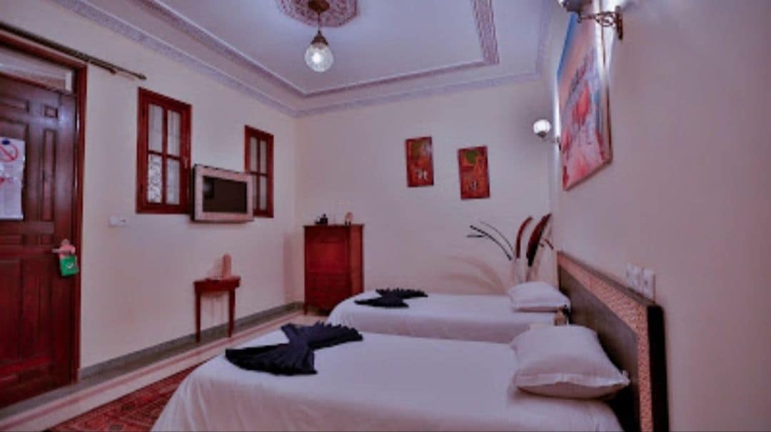 A hotel room with two beds, a television, a red cabinet, and a door with a red handle.