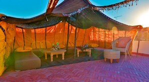 A tented outdoor seating area with a cushioned bench, a small table, and a wicker chair.