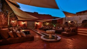 An outdoor lounge area with multiple seating arrangements, including sofas and chairs, under a large canopy.