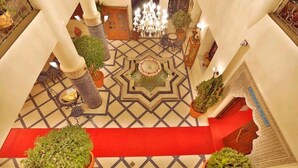 A spacious lobby with a patterned floor, a central fountain, and a red carpet leading to a staircase.