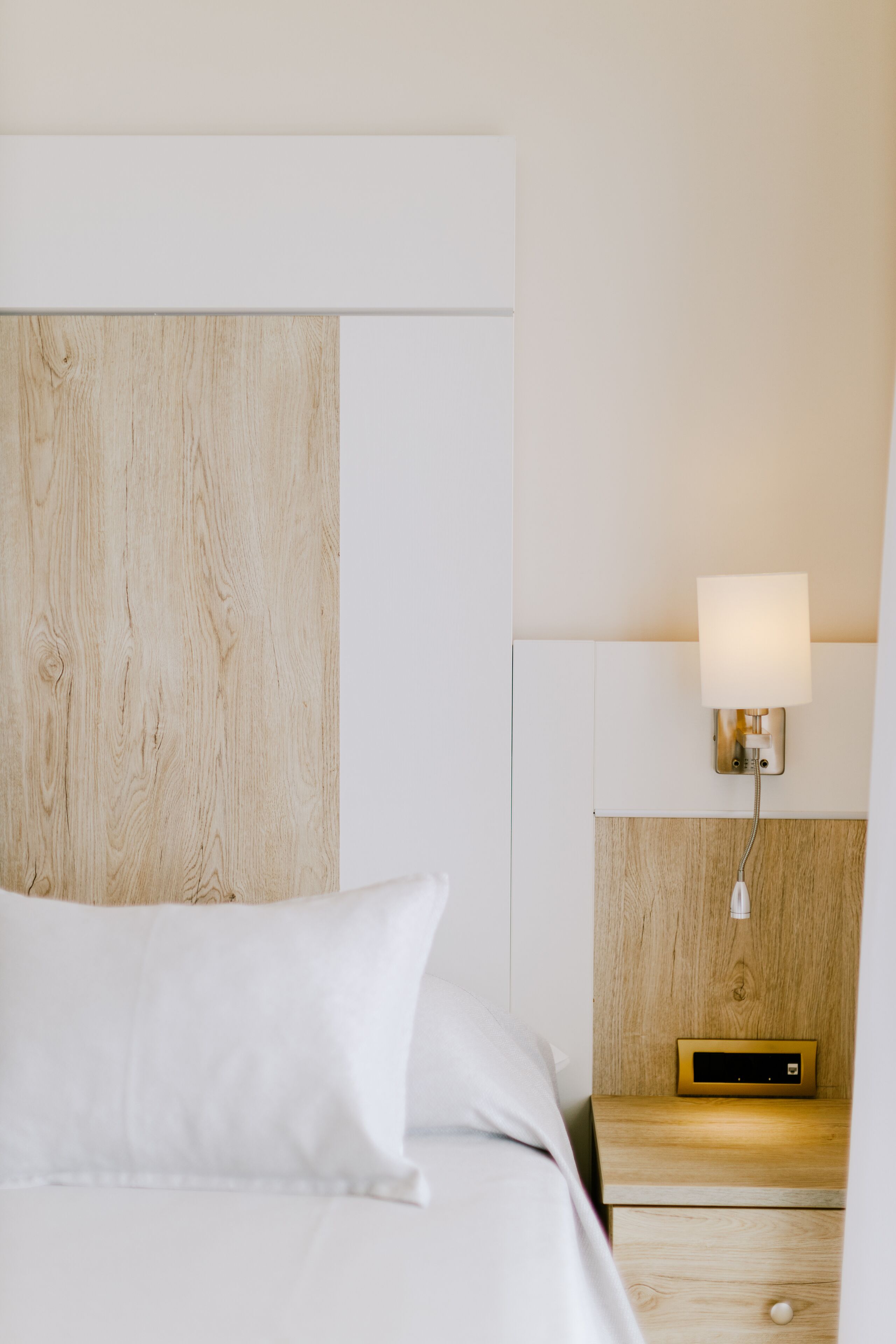 A hotel room with a wooden headboard, a bedside table with a lamp, and a digital clock.