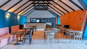 A modern restaurant with a high ceiling, exposed beams, and a mix of seating options including tables and a pink sofa.