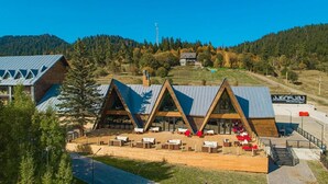 A modern lodge with a triangular roof design, outdoor seating area, and a view of a forested hillside.
