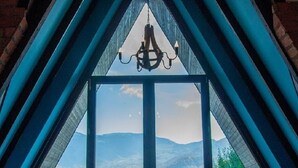 A room with a large window offering a view of a valley and mountains. There are two chairs and a chandelier.