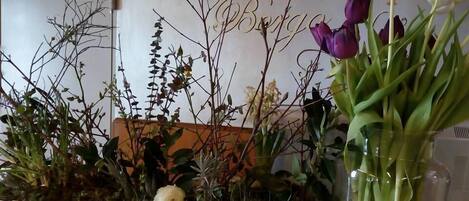 Un arrangement floral composé de différentes plantes et fleurs, notamment des tulipes violettes et blanches, dans un vase en verre posé sur un comptoir.