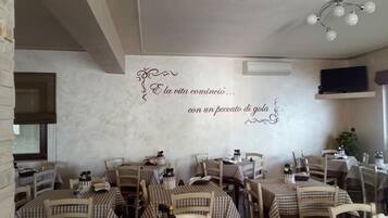 L’intérieur d’un restaurant avec des nappes à carreaux, des chaises en bois et un mur décoratif orné de texte en italien.
