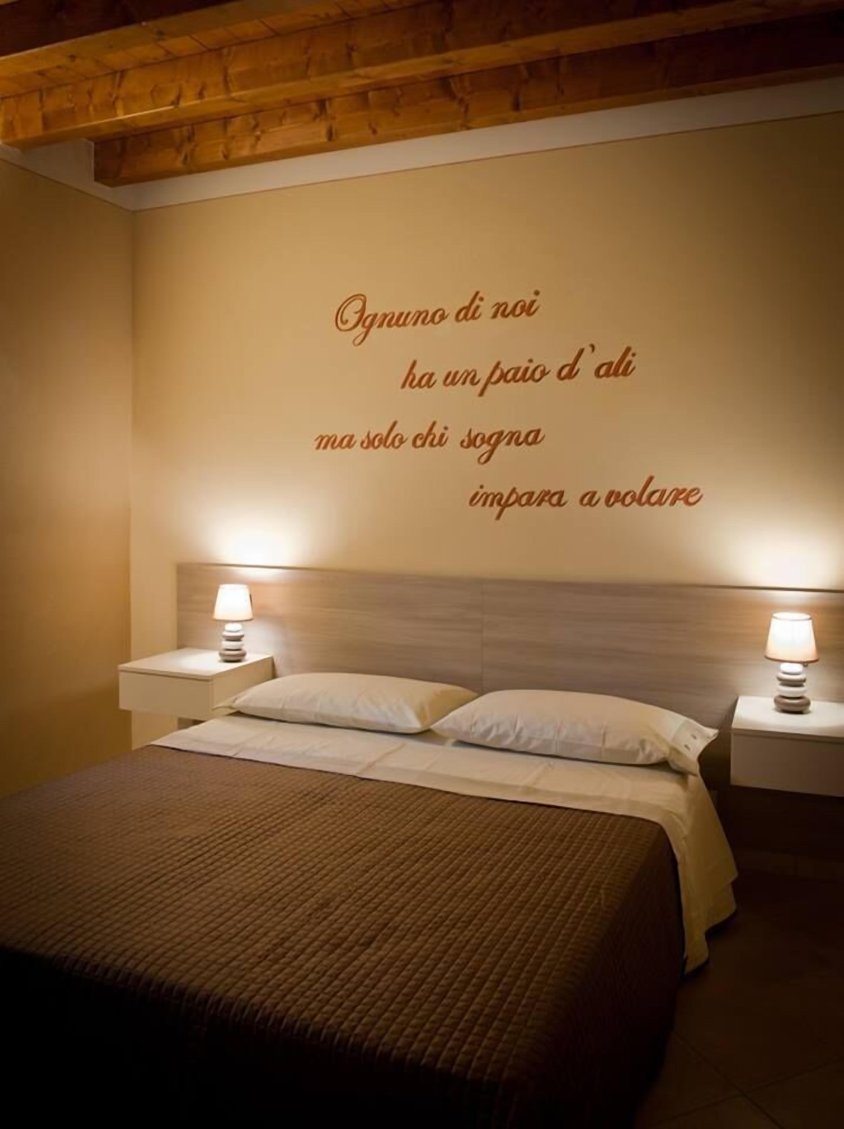 Ein Schlafzimmer mit einem Bett, zwei Nachttischlampen und einer Wand mit einem Zitat in Italienisch.