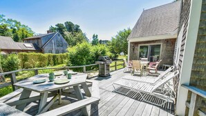 Een houten terras met een picknicktafel, buitenmeubels en een barbecue.