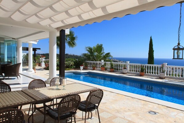 A poolside area with a table and chairs, a white railing, and a view of the sea. - Villa Azalea - Exclusive villa with unique mediterranean view (Mijas Costa)