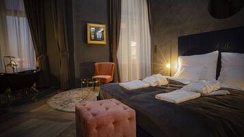 Una camera d'hotel con un grande letto, un pouf rotondo, una sedia, una scrivania con uno specchio e un quadro appeso al muro.