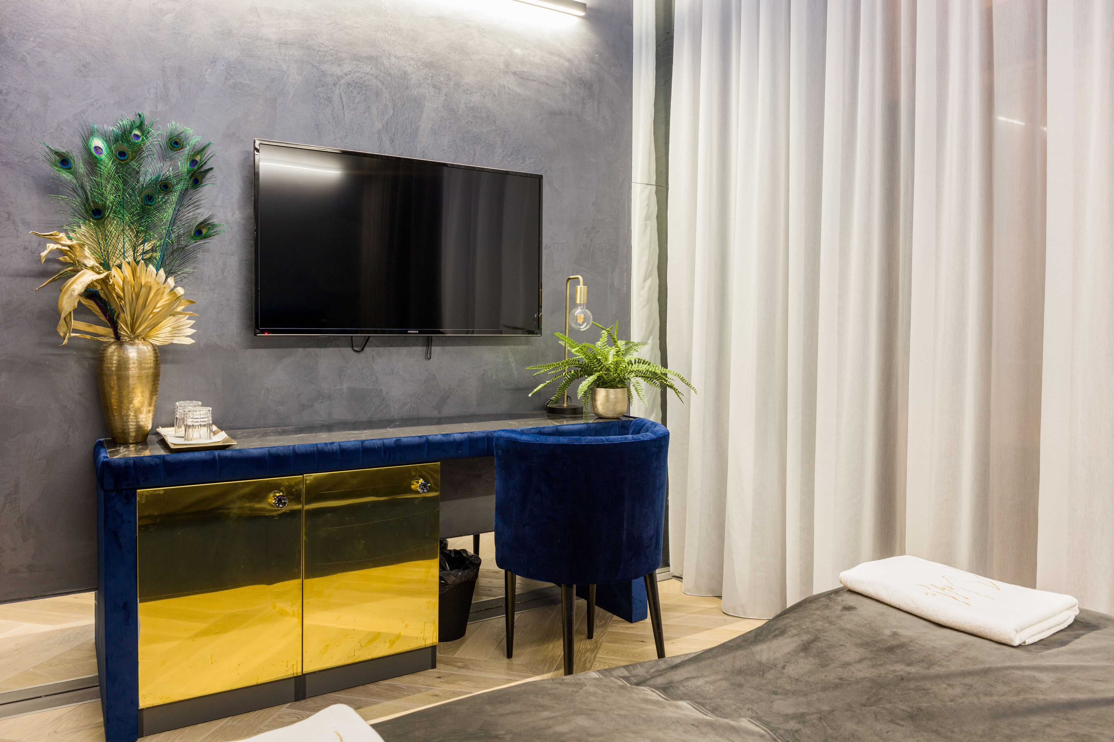 Een moderne kamer met een blauwe fluweelstoel, een zwart-gouden kast, een flatscreen-tv en een decoratieve plant.