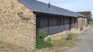 Een gebouw van baksteen met een donker dak en een bord waarop staat: 'Decoy Farm Cottages'.