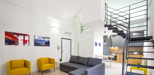 A modern living area with a grey sectional sofa, yellow armchairs, and a staircase with a metal railing.