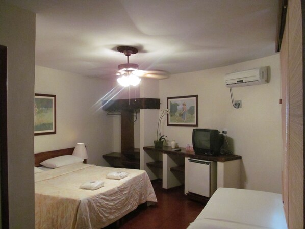 Une chambre d’hôtel équipée d’un lit, d’un bureau avec une télévision, d’un ventilateur de plafond et d’un appareil de climatisation.