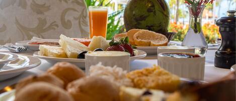 Una mesa con alimentos para el desayuno, como pan, frutas y un vaso de jugo de naranja.