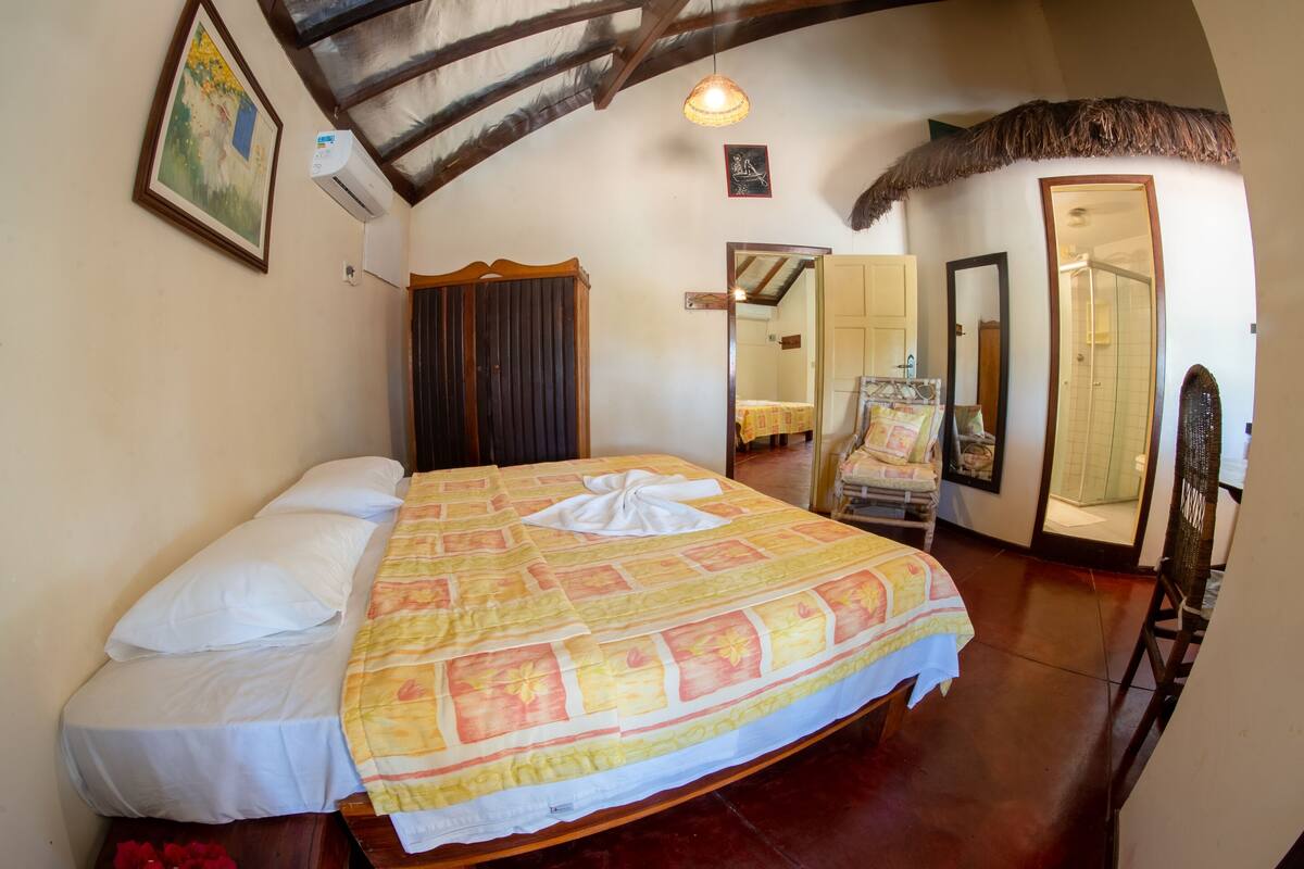 A bedroom with a large bed, a wooden wardrobe, a mirror, and a ceiling fan.