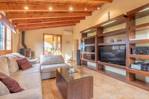 A living room with a sofa, a glass coffee table, wooden shelves, and a television. - Fantastic Finca with Wi-Fi, Air Conditioning, Garden and Terrace (Algaida)