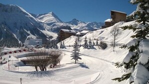 A snow-covered ski resort with a mountain backdrop, a ski lift, and a building with a sloped roof.