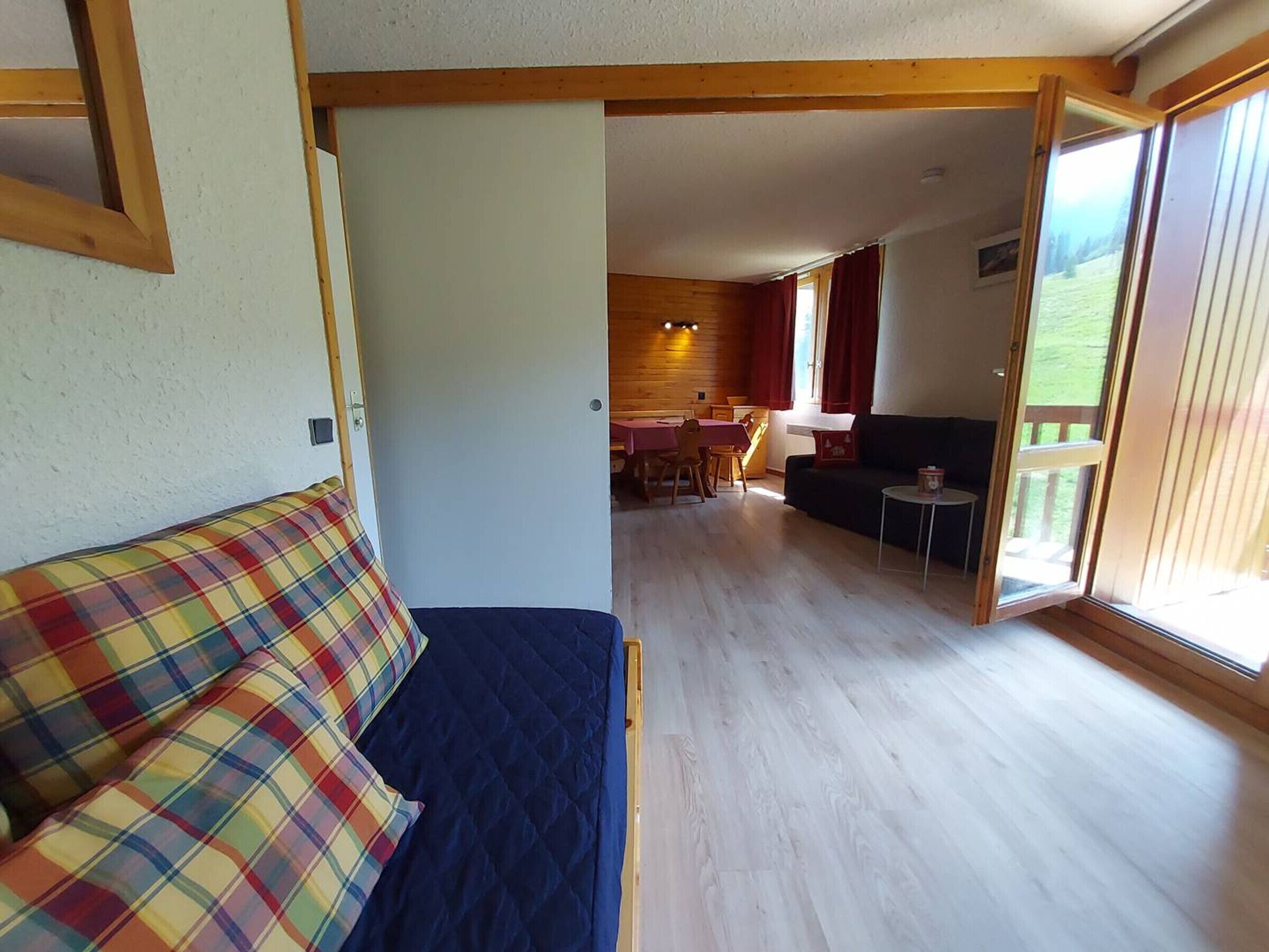 A room with a bed, a sofa, a dining area, and a sliding glass door leading to an outdoor area.