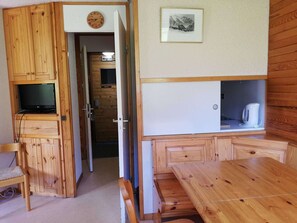 Een houten blokhut van binnen, met een televisie, een wit kastje, een houten tafel en een stoel.