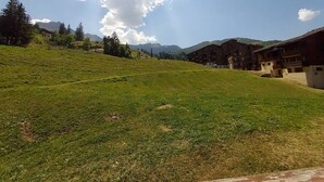 Une colline verdoyante, avec un ensemble de bâtiments en arrière-plan.