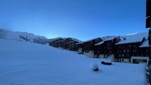 Une station de ski enneigée, avec des bâtiments à plusieurs étages, une piste de ski et des montagnes en arrière-plan.