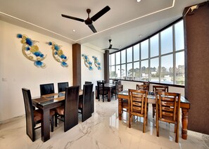 A spacious dining area with a high ceiling, large windows, and decorative wall art. - Shri Vyas HomeStay-Tranquility & Peace in Elegance (Rishikesh)