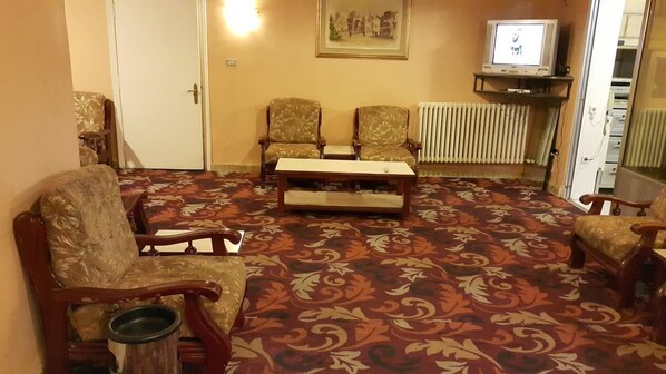 A living room with a patterned carpet, two armchairs, a wooden coffee table, and a television on a stand. - Nefertiti Hotel (Amman)