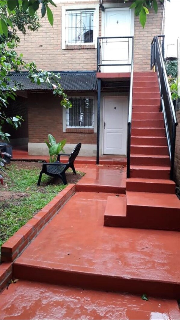 Un escalier menant à une porte, le tout entouré d’un mur de briques et de verdure.