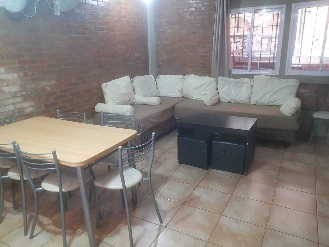 Een eetgedeelte met een houten tafel en stoelen, een bank met kussens, en een zwarte kast.
