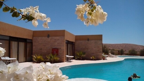 A pool area with a clear blue pool, lounge chairs, and a building with a stone facade.
