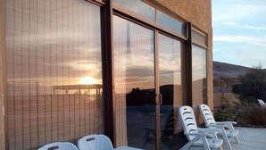 A patio with a table and chairs, a sliding glass door, and a view of the sunset.