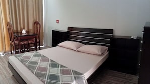 A neatly made bed with a plaid bedspread and two pillows, a wooden nightstand with a lamp, and a small table with a chair.
