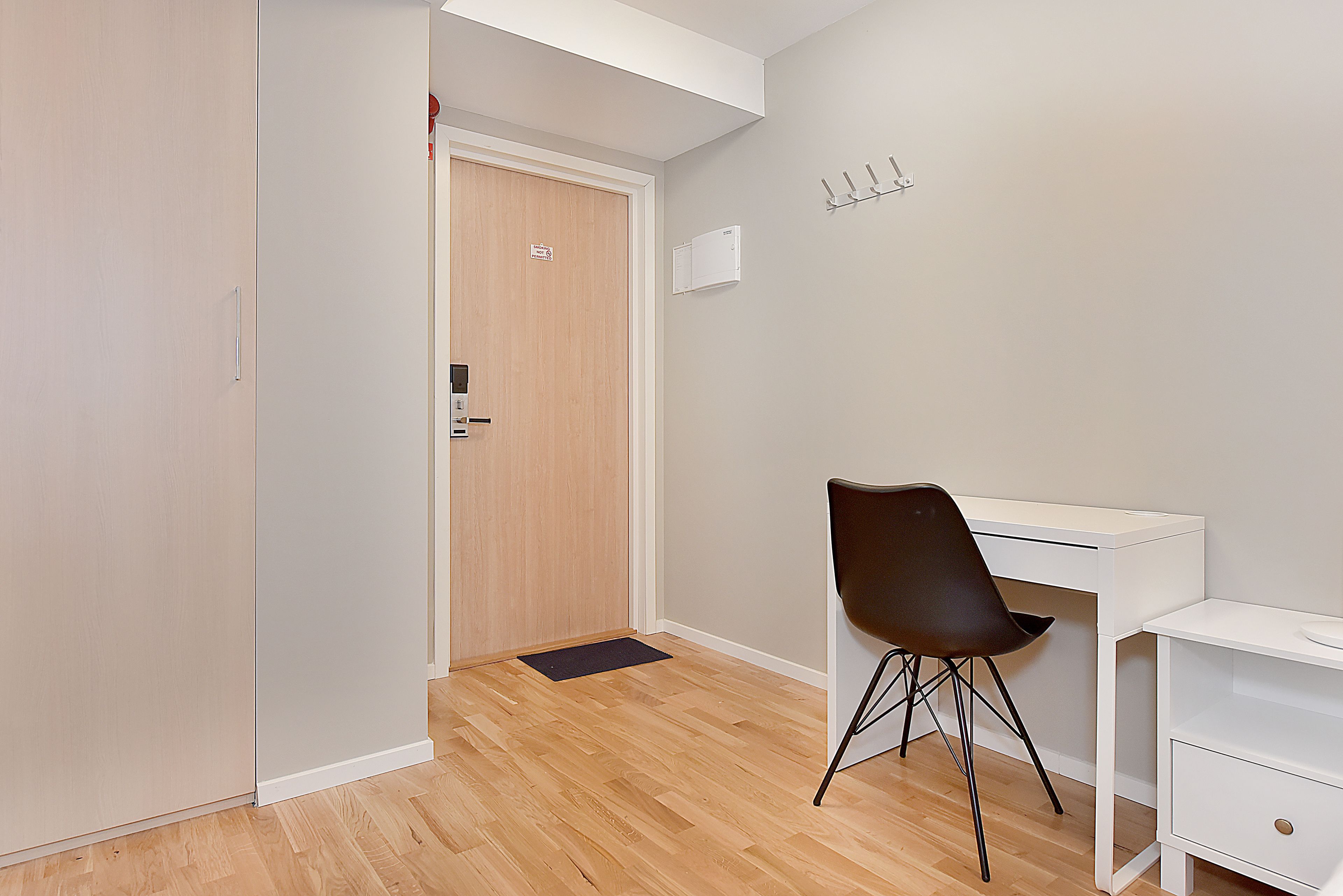 A room with a wooden floor, a white desk, a black chair, a white wardrobe, and a door with a handle.
