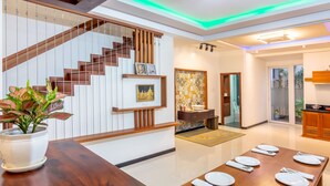 A modern dining area with a wooden table set for six, a staircase with wooden railings, and a kitchen visible in the background. - Pretty 4BR House@3MIN to the beach@ 3N Free pickup (Sơn Trà)