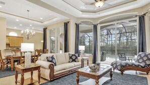 A spacious living room with a sofa, armchairs, a coffee table, and a chandelier. - A Rare Find! Lely Resort Single Family Home in Prestigious Majors Community (Naples)