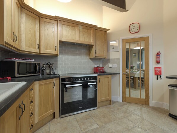 A kitchen with wooden cabinets, a microwave, a toaster, and a stove. - Harbour View - UKC2303 (Wainfleet St. Mary, near Skegness)