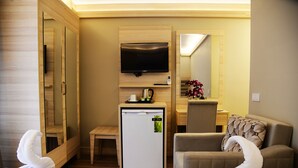Ein Hotelzimmer mit Flachbildfernseher an der Wand, einem kleinen Kühlschrank, einer Kaffeemaschine, einem Sofa und einem Sessel.