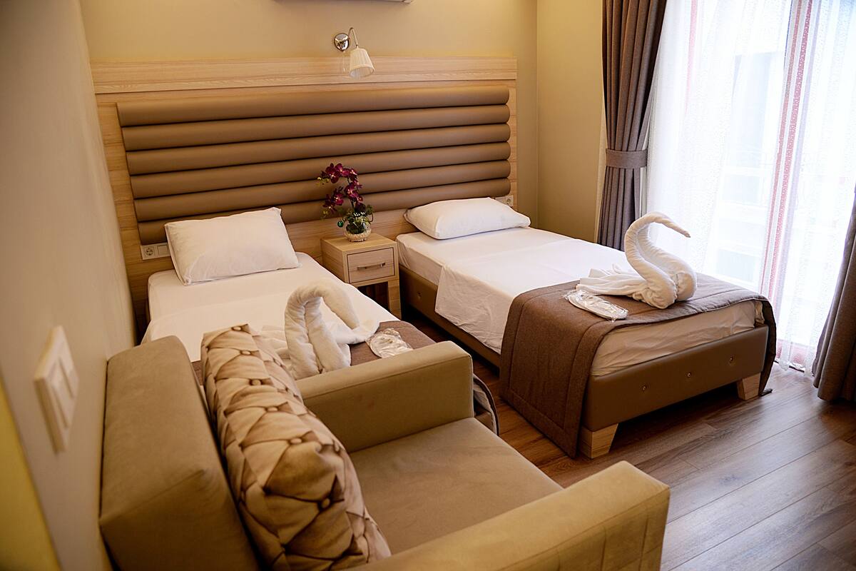 A hotel room with two beds, a sofa, a nightstand, and a window with curtains.