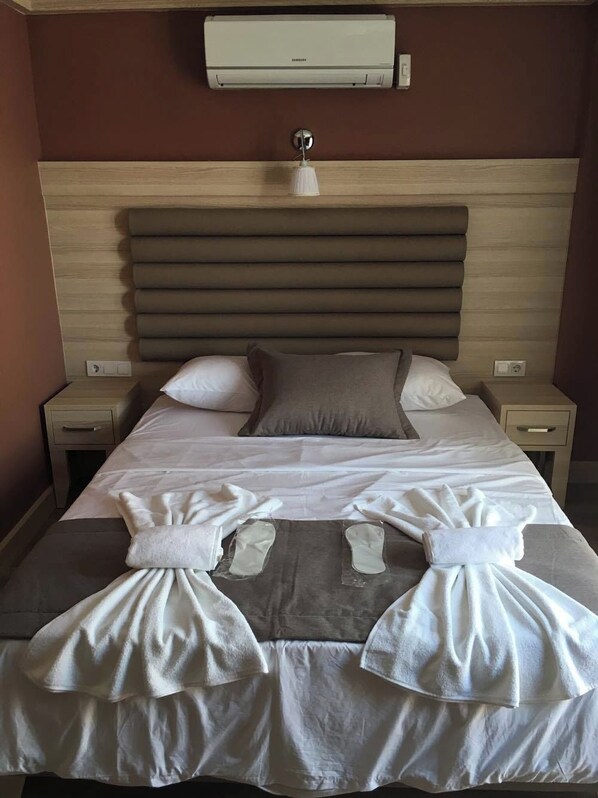 A hotel room with a wooden headboard, a bed with white linens, two bedside tables, and an air conditioning unit above the bed. - Al Khaleej (Istanbul)