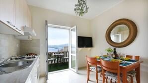 A modern kitchen with a large window, a dining area with a round mirror, and a view of a lake. - Villa Korkyra with Pool (Lumbarda)